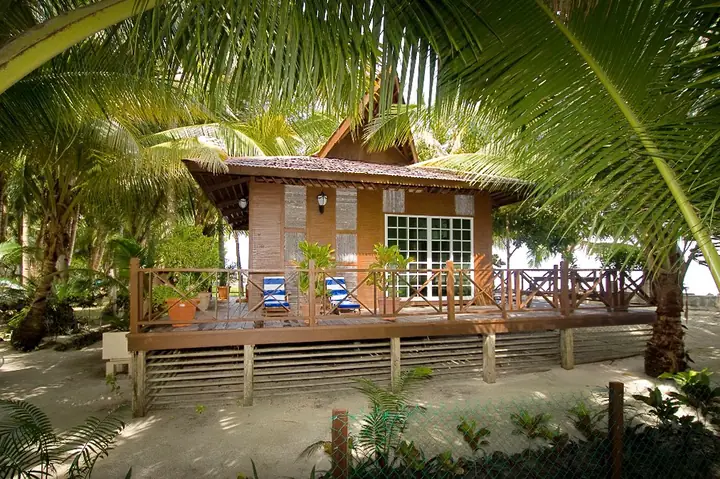 Suite Chalet at Sipadan-Mabul Resort: timber chalet with a wide verandah and deck chairs, under coconut palms beside the sand